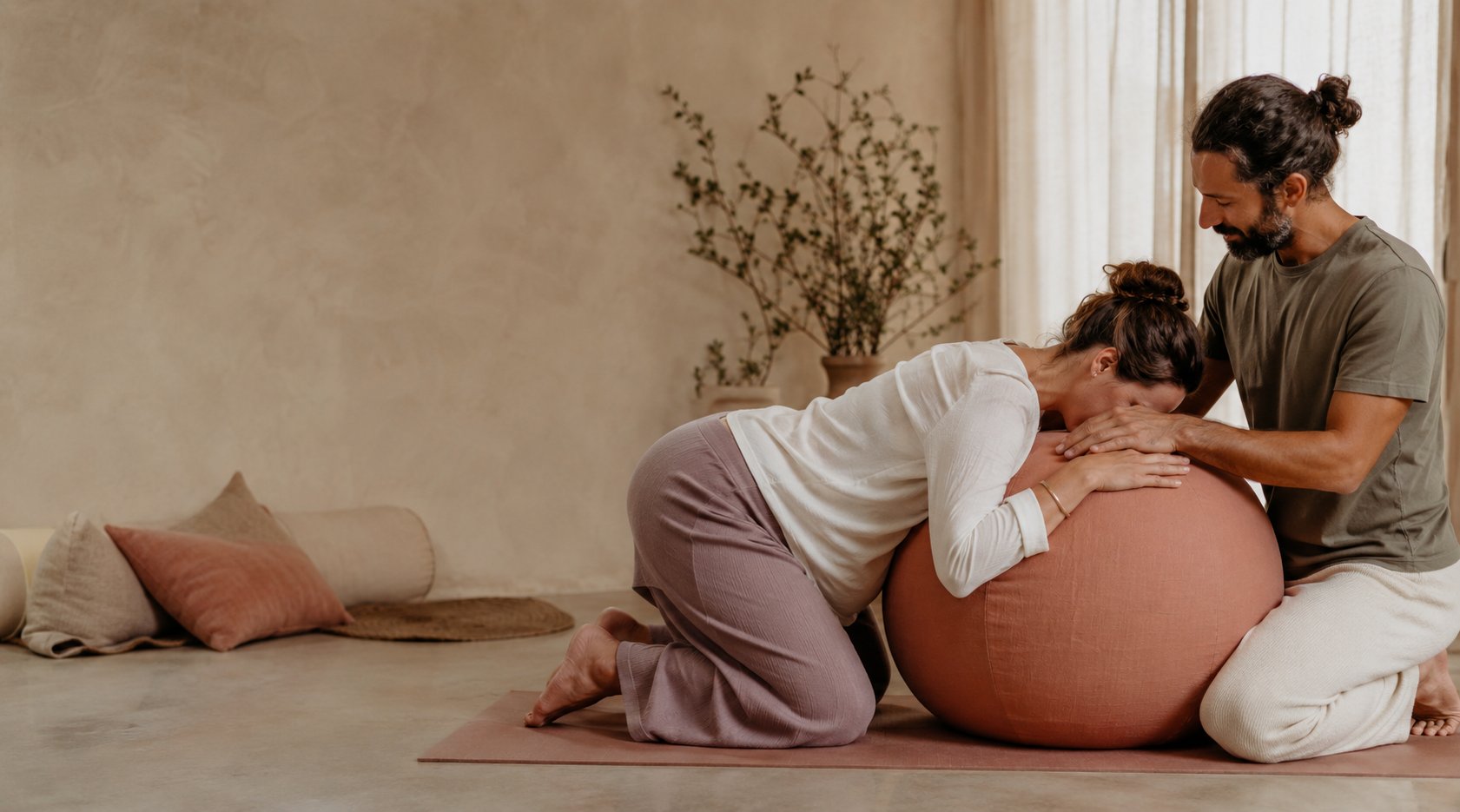 A pregnant woman leaning on a birth ball while her partner supports her